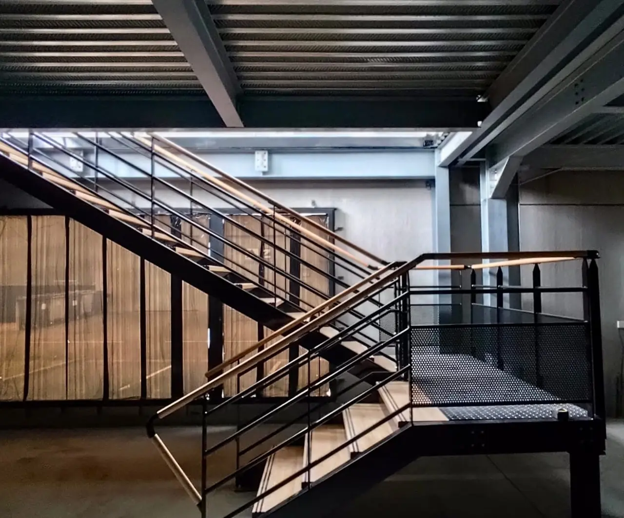 Black steel staircase with wooden treads leading to an office mezzanine